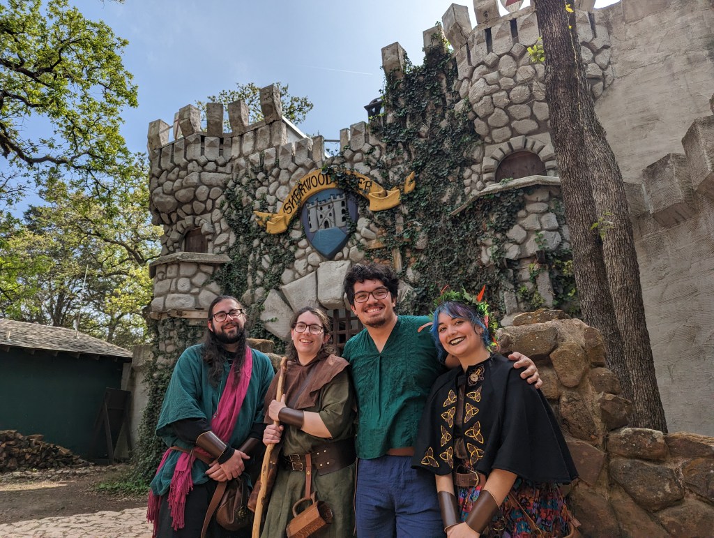 Image of the This Could Get Dicey group in front of a castle-like structure wearing renfaire garb. From left to right: Alex, Becky, Kenny, Destanie.